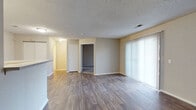 This single-floor unit offers a practical and well-organized layout designed for comfortable everyday living. The living area is generously proportioned, featuring durable wood-look plank flooring, neutral beige walls, and a textured ceiling. A large sliding glass door fitted with vertical blinds allows natural light to fill the space and provides outdoor access. The open-concept design connects the living area to the kitchen via a peninsula-style breakfast bar, offering both separation and visual continuity.

The kitchen is equipped with white cabinetry, a black coil-burner electric range with overhead exhaust hood, a refrigerator, and ample counter space. Conveniently tucked adjacent to the kitchen is an in-unit laundry area housing a washer and dryer.

The bedrooms are carpeted in a neutral gray tone and feature textured ceilings with ceiling-mounted HVAC vents. One bedroom includes a window with natural views, while another presents a more private, enclosed feel. Both rooms offer a clean, move-in-ready appearance with ample wall space for furniture arrangements.

The bathroom includes a full tub and shower combination with white tile surround, brushed nickel fixtures, and wood-look flooring that coordinates with the rest of the unit. Overall, this space presents a clean, functional, and cohesive interior with consistent finishes throughout.