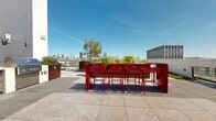 Located at 830 Eddy Street in San Francisco's Lower Nob Hill neighborhood, this rooftop terrace offers a thoughtfully designed outdoor retreat with sweeping 360-degree views of the San Francisco skyline, the distant hills, and beyond. The terrace is finished with large-format stone tiles that lend a clean, modern aesthetic throughout the generous open-air space.

A standout feature is the vibrant red high-top bar station, complete with matching red barstools, which serves as a bold social focal point against the backdrop of the downtown skyline—including a glimpse of the Transamerica Pyramid. Surrounding the bar area, raised Cor-Ten steel planters are filled with a diverse mix of trees, palms, succulents, and flowering plants, adding warmth, texture, and a lush, garden-like atmosphere.

The terrace is organized into multiple distinct zones: a casual lounge area furnished with comfortable outdoor sofas and coffee tables, a dining area with bistro-style tables and chairs shaded by mature trees, and open promenades ideal for entertaining or relaxed strolling. Low-profile living green walls and ground-level planted beds line the perimeter, softening the boundary walls while contributing to the space's verdant character.

Recessed step lighting is integrated throughout, ensuring the terrace is equally inviting after dark. The result is a well-appointed, multi-functional outdoor space designed for community gathering and urban enjoyment.