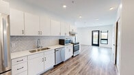 Located at 155 Jackson St in Oshkosh, WI, this modern 2-bedroom, 1-bathroom unit offers a well-designed, single-floor layout with contemporary finishes throughout. Warm wood-look luxury vinyl plank flooring flows consistently across all rooms, complementing the clean white walls and creating a bright, cohesive aesthetic.

The open-concept kitchen and dining area serves as the heart of the unit, featuring white shaker cabinetry with black hardware, a herringbone-patterned tile backsplash, white quartz countertops, a stainless steel sink, and a full suite of stainless steel appliances including a refrigerator, gas range, dishwasher, and microwave. Recessed lighting illuminates the space, which opens directly to the main living and entry areas.

Both bedrooms are generously proportioned with crisp white walls and large black-framed windows that bring in natural light and neighborhood views. The primary bedroom includes a spacious walk-in closet outfitted with wire shelving systems, offering substantial storage capacity. An additional closet serves the second bedroom.

The bathroom is equipped with an accessible roll-in shower featuring stainless steel grab bars, a handheld showerhead, and a fold-down bench, reflecting a thoughtful, inclusive design. A dedicated laundry area and a private balcony with glass railings round out the unit's practical amenities.