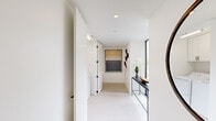 This thoughtfully designed single-floor residence offers a clean, contemporary aesthetic throughout, defined by a crisp white palette, light flooring, and black-framed windows that frame abundant natural light and outdoor views. The open-plan kitchen and living area serves as the heart of the home, where a well-appointed kitchen features two-tone cabinetry — white uppers paired with gray lowers — stainless steel appliances, a white tile backsplash, and generous counter space. The adjoining living and dining area is bathed in natural light through large floor-to-ceiling windows and a sliding glass door that opens to an outdoor balcony, offering leafy neighborhood views. Three bedrooms provide comfortable accommodations, each with a clean, serene atmosphere. The spacious primary bedroom includes a well-organized walk-in closet with custom shelving and hanging space. A second bedroom also features built-in closet storage. Both bathrooms are finished in neutral tones with large-format tile; one bath includes a floor-to-ceiling window with treetop views. A dedicated laundry room with side-by-side washer and dryer and overhead cabinetry adds everyday convenience. Throughout, the hallways are bright and minimal, accented with tasteful wall art and slim console furniture.