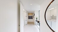 This thoughtfully designed single-floor residence offers a clean, contemporary aesthetic throughout, defined by a crisp white palette, light flooring, and black-framed windows that frame abundant natural light and outdoor views. The open-plan kitchen and living area serves as the heart of the home, where a well-appointed kitchen features two-tone cabinetry — white uppers paired with gray lowers — stainless steel appliances, a white tile backsplash, and generous counter space. The adjoining living and dining area is bathed in natural light through large floor-to-ceiling windows and a sliding glass door that opens to an outdoor balcony, offering leafy neighborhood views. Three bedrooms provide comfortable accommodations, each with a clean, serene atmosphere. The spacious primary bedroom includes a well-organized walk-in closet with custom shelving and hanging space. A second bedroom also features built-in closet storage. Both bathrooms are finished in neutral tones with large-format tile; one bath includes a floor-to-ceiling window with treetop views. A dedicated laundry room with side-by-side washer and dryer and overhead cabinetry adds everyday convenience. Throughout, the hallways are bright and minimal, accented with tasteful wall art and slim console furniture.