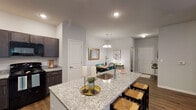 Located at 7405 Fegenbush Ln in Louisville, KY, this single-floor residence offers a well-designed, open-concept layout that maximizes both functionality and comfort. The kitchen is a standout feature, showcasing rich dark cabinetry, granite countertops, recessed lighting, and a full suite of black appliances including a refrigerator, range, and microwave. A granite-topped island with bar seating serves as the centerpiece, seamlessly connecting the kitchen to the adjacent dining and living areas. The dining area is defined by warm wood-look flooring and an elegant chandelier overhead, creating an inviting space for gatherings. The living room offers a relaxed, open feel with a ceiling fan, recessed lighting, and a door providing access to an exterior patio or entry. Two well-appointed bedrooms feature plush carpeting and generous windows that allow for natural light. The primary bedroom includes wall-mounted sconce lighting and access to a private bathroom. A second full bathroom features a granite-topped vanity with dark cabinetry and a tub-shower combination. Throughout the residence, neutral gray walls, wood-look vinyl flooring, and clean architectural lines contribute to a cohesive, modern aesthetic that is both practical and stylish.
