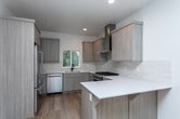 Located at 6236 W State St in Boise, Idaho, this modern two-story home showcases clean design and quality finishes throughout. Wide-plank hardwood flooring flows through the main living areas, complemented by crisp white walls and recessed lighting that create a bright, airy atmosphere. The contemporary kitchen is a standout feature, equipped with stainless steel appliances including a gas range with a stainless hood, a dishwasher, and a refrigerator. Light wood cabinetry, white quartz countertops, a subway tile backsplash, and a peninsula with additional cabinetry complete the thoughtfully designed space. A sliding glass door in the upper-level living area opens to a balcony with cable railing, offering serene views of the surrounding natural landscape. Bathrooms are finished with a consistent design language, featuring light wood vanities, white countertops, and bold matte black fixtures. The full bathrooms include white subway-tiled shower and tub surrounds with stone tile flooring, while a convenient half bath offers continuity in style. Bedrooms are carpeted for comfort, with large windows drawing in natural light and outdoor views. A carpeted staircase with a warm wood handrail connects the two floors, tying the home's modern aesthetic together seamlessly.