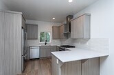 Located at 6236 W State St in Boise, Idaho, this modern two-story home showcases clean design and quality finishes throughout. Wide-plank hardwood flooring flows through the main living areas, complemented by crisp white walls and recessed lighting that create a bright, airy atmosphere. The contemporary kitchen is a standout feature, equipped with stainless steel appliances including a gas range with a stainless hood, a dishwasher, and a refrigerator. Light wood cabinetry, white quartz countertops, a subway tile backsplash, and a peninsula with additional cabinetry complete the thoughtfully designed space. A sliding glass door in the upper-level living area opens to a balcony with cable railing, offering serene views of the surrounding natural landscape. Bathrooms are finished with a consistent design language, featuring light wood vanities, white countertops, and bold matte black fixtures. The full bathrooms include white subway-tiled shower and tub surrounds with stone tile flooring, while a convenient half bath offers continuity in style. Bedrooms are carpeted for comfort, with large windows drawing in natural light and outdoor views. A carpeted staircase with a warm wood handrail connects the two floors, tying the home's modern aesthetic together seamlessly.