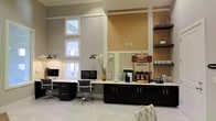 Located at 75 Cross Creek Pkwy in Hattiesburg, Mississippi, this single-story community space is designed to provide residents and visitors with a comfortable, functional environment. The interior is finished with a clean, contemporary aesthetic, featuring soaring ceilings that amplify the sense of openness and allow natural light to pour in through stacked transom-style windows along the walls.

The business center area offers a built-in workstation with ample counter space, accommodating multiple desktop computers and ergonomic chairs — ideal for residents who need a quiet place to work or study. Adjacent to the workstation is a dedicated refreshment station stocked with a Community Coffee brewer and a variety of coffee supplies, providing a welcoming touch for residents and guests alike. Dark cabinetry with chrome hardware lines the base of this counter, offering generous storage while creating a polished visual contrast against the light-toned countertop.

The walls are painted in warm neutral tones, complemented by wainscoting-style paneling details that add architectural character to the space. Open shelving units flank the accent wall, providing both display and storage functionality. The light tile flooring ties the space together, reinforcing the bright, airy atmosphere throughout. Overall, the space balances practicality with inviting design.
