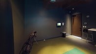 This dedicated indoor golf simulator room is thoughtfully designed to deliver an immersive golfing experience in a controlled environment. The space is finished with deep charcoal-toned walls and a dark ceiling, creating a focused, distraction-free atmosphere that enhances the visual impact of the simulation system.

At the heart of the room is a High Definition Golf simulator, featuring a large projection screen framed by black curtain surrounds that span the full width of one wall. The ceiling-mounted projector delivers crisp, high-resolution imagery of world-class golf courses, transporting players to realistic virtual environments. A secondary wall-mounted monitor is positioned to the side, providing additional game data and scoring information during play.

The flooring consists of a dual-tone artificial turf hitting mat — a green strip laid over a broader yellow-green surface — providing a realistic feel underfoot for each shot. A golf bag with clubs stands ready near the hitting area, and golf balls are conveniently staged on the floor.

A bistro-style table with bar stools is positioned near the rear of the room, offering a comfortable spot for spectators or players to relax between rounds. The overall ambiance is intimate and purpose-built, making this simulator room an ideal venue for practice, entertainment, or competitive play year-round.