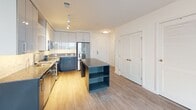 Located at 1250 Half St SE in Washington, DC's vibrant Navy Yard neighborhood, this single-floor unit showcases a clean, contemporary design throughout. Light-toned luxury vinyl plank flooring runs continuously across the open-concept living and dining area, creating a bright, cohesive aesthetic complemented by crisp white walls and modern recessed lighting.

The kitchen is a standout feature, outfitted with two-tone cabinetry — white upper cabinets with blue-grey lower cabinets — paired with a speckled stone countertop and a matching mosaic tile backsplash. A full suite of stainless steel appliances, including a french-door refrigerator, electric range with microwave, and dishwasher, adds a polished, functional finish. A center island with open shelving and a stone countertop provides additional prep and storage space.

The living area is generously proportioned, benefiting from natural light through large black-framed windows that frame views of the surrounding cityscape. The bedroom continues the light wood flooring and neutral palette, with an oversized window providing ample daylight.

The bathroom features a vessel sink atop a dark, stone-topped vanity with drawer storage, a large frameless mirror, and an open wall-mounted shelving unit — combining modern style with practical organization. The overall ambiance is clean, minimal, and move-in ready.