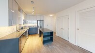 Located at 1250 Half St SE in Washington, DC's vibrant Navy Yard neighborhood, this single-floor unit showcases a clean, contemporary design throughout. Light-toned luxury vinyl plank flooring runs continuously across the open-concept living and dining area, creating a bright, cohesive aesthetic complemented by crisp white walls and modern recessed lighting.

The kitchen is a standout feature, outfitted with two-tone cabinetry — white upper cabinets with blue-grey lower cabinets — paired with a speckled stone countertop and a matching mosaic tile backsplash. A full suite of stainless steel appliances, including a french-door refrigerator, electric range with microwave, and dishwasher, adds a polished, functional finish. A center island with open shelving and a stone countertop provides additional prep and storage space.

The living area is generously proportioned, benefiting from natural light through large black-framed windows that frame views of the surrounding cityscape. The bedroom continues the light wood flooring and neutral palette, with an oversized window providing ample daylight.

The bathroom features a vessel sink atop a dark, stone-topped vanity with drawer storage, a large frameless mirror, and an open wall-mounted shelving unit — combining modern style with practical organization. The overall ambiance is clean, minimal, and move-in ready.