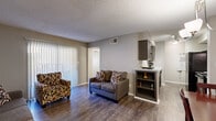 This well-organized two-bedroom, one-bathroom residence is laid out on a single floor, offering a functional and cohesive living environment. The open-concept living and dining area forms the heart of the home, featuring durable wood-style flooring, neutral wall tones, and a textured ceiling. A sliding glass door in the living room floods the space with natural light and provides access to an outdoor area, while vertical blinds offer privacy control. A dedicated dining nook, illuminated by a stylish chandelier, sits adjacent to the living area and flows directly into the galley-style kitchen. The kitchen is equipped with dark espresso cabinetry, granite-style countertops, black appliances including a range, microwave, and refrigerator, and track lighting overhead. The primary bedroom features plush carpeting, a ceiling fan, and a large window that brings in ample natural light. The second bedroom is similarly appointed with carpet flooring and window access. The shared full bathroom includes a tub-shower combination with tile surround, a dark vanity with stone-style countertop, and wood-style flooring. A closet provides additional storage. The overall aesthetic is cohesive and practical, with consistent finishes throughout.