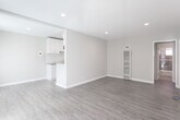 Located at 11424 Killion St in Los Angeles, CA, this single-floor residence offers a clean, modern aesthetic with a practical and comfortable layout. The living area is open and airy, featuring warm wood-look laminate flooring, neutral warm-gray walls, recessed lighting, and a wall-unit heater and air conditioner, ensuring year-round comfort. Large windows dressed with vertical blinds fill the space with natural light and offer views of the surrounding greenery. The entry area welcomes you with a full-lite front door alongside sliding glass doors, further enhancing the sense of openness. The kitchen is semi-open to the living space, separated by a half-wall partition that adds architectural interest while maintaining visual connectivity. It is outfitted with white cabinetry, granite-style countertops, a white subway tile backsplash, a stainless steel gas range, a range hood, and a full-size refrigerator, all set on clean tile flooring. The bedroom is generously proportioned, featuring the same warm laminate flooring, recessed lighting, and a large window with vertical blinds that invites ample natural light. Throughout, the space maintains a consistent, freshly updated palette that conveys a bright and welcoming atmosphere.