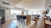 Located on Bank Street in New London, Connecticut, this thoughtfully designed single-floor amenity lounge offers a dynamic and inviting space for socializing and recreation. The open-concept layout is anchored by rich hardwood flooring that flows seamlessly throughout, unifying the distinct activity zones. At the heart of the space, a substantial natural wood bar island with pendant lighting and bar seating serves as a central gathering point, complemented by a striking teal mosaic tile backsplash behind the kitchenette area. Large windows line the perimeter, flooding the interior with abundant natural light and offering open views of the surrounding New London skyline. The billiards area features a prominently placed pool table set against a bold teal accent wall with classic wainscoting, wall-mounted artwork, and a flat-screen TV, creating an energetic yet polished entertainment zone. A dedicated lounge area provides comfortable seating arrangements with plush sofas, accent chairs, and a geometric area rug, ideal for conversation or casual viewing. An additional TV lounge nook with a large wall-mounted screen and flexible seating offers a more intimate entertainment experience. The overall ambiance blends coastal-inspired accents with contemporary design, making this a versatile and welcoming communal destination.