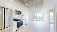Located at 30 Rue Jos-Montferrand in Gatineau, this contemporary 2-bedroom, 2-bathroom unit showcases an industrial-modern aesthetic defined by its signature exposed concrete ceiling, which contrasts beautifully against crisp white walls and light-toned wood-style flooring throughout. The open-concept living and kitchen area forms the heart of the unit, where large floor-to-ceiling windows flood the space with natural light while framing elevated views of the surrounding cityscape.

The kitchen is well-appointed with white cabinetry, stainless steel appliances including a refrigerator, electric range, built-in microwave, and dishwasher, complemented by a undermount sink and ample counter space. The living area flows seamlessly from the kitchen, creating a functional and airy shared space.

Both bedrooms are bright and well-proportioned, each featuring large windows with city views and light wood flooring. The primary bedroom includes sliding closet doors for efficient storage. The two bathrooms are finished with large-format neutral tiles; one features a soaking tub with tiled surround, while the other offers a sleek glass-enclosed walk-in shower. The overall ambiance is clean, minimalist, and contemporary.