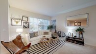 This single-floor residence offers a thoughtfully arranged layout with a warm, neutral aesthetic carried consistently throughout each room. The living area serves as the centerpiece of the home, featuring large windows that frame outdoor greenery and flood the space with abundant natural light. Soft carpeting, a striped area rug, and eclectic wall art contribute to a cozy yet stylish atmosphere.

Adjacent to the living area is a dedicated dining nook, illuminated by track lighting and positioned alongside a window and a glass-panel door that provides direct outdoor access, ideal for seamless indoor-outdoor living.

The kitchen features light wood cabinetry, white appliances, and a peninsula with bar seating that enhances functionality while creating an open connection to the surrounding living spaces. Recessed skylighting adds brightness to the work area.

The bedroom is a serene retreat with plush carpeting, a large window offering wooded views, and ample wall space. The room is well-proportioned and benefits from natural light throughout the day.

The bathroom is cleanly finished with light tile flooring, a wide vanity with wood-toned cabinetry, a large mirror, and neutral walls. Overall, the residence presents a cohesive, livable design with practical features and a calming atmosphere.