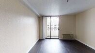 Located at 118 Paseo De San Antonio in the heart of San Jose, California, this single-floor studio unit offers a well-organized, open-concept layout designed to maximize functionality and comfort. The main living area is finished with rich, dark hardwood-style flooring that runs throughout the entire unit, providing a clean and modern aesthetic against the neutral, warm-toned walls and textured ceiling.

A defining feature of the living space is the full-width sliding glass door that opens onto a private balcony, allowing an abundance of natural light to fill the room while offering open views of the surrounding urban neighborhood. A wall-mounted PTAC heating and cooling unit ensures year-round climate control.

The compact kitchenette is neatly integrated into the unit, featuring white cabinetry, a coil electric range, an over-the-range microwave, a single-basin sink, and a compact refrigerator — all set beneath light stone-toned countertops. An electrical panel is conveniently recessed into the wall near the entryway.

The bathroom is thoughtfully appointed with dark hardwood-style flooring consistent with the rest of the unit, a wide vanity with an undermount sink, generous mirror, white cabinetry, and accessibility-friendly grab bars. The overall design of the unit is clean, practical, and well-suited for urban living in downtown San Jose.