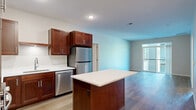 Located at 1875 Paulson Rd in River Falls, Wisconsin, this 2-bedroom, 1-bathroom residence offers a thoughtfully designed single-floor layout. The open-concept kitchen and living area serves as the heart of the space, showcasing rich dark wood cabinetry, white quartz countertops, a central island, and a full suite of stainless steel appliances including a refrigerator, dishwasher, microwave, and range. Light wood-tone flooring runs throughout the main living areas, enhancing the bright and clean aesthetic. The living room is generously sized and features sliding glass doors that open onto a private balcony, offering views of the surrounding greenery. The primary bedroom is a comfortable retreat with direct balcony access and wood-tone flooring. The second bedroom features soft carpeting and a closet, making it well-suited as a guest room or home office. The full bathroom is finished with wood-look tile flooring, a single vanity with a clean white countertop, a large mirror, and a tub-shower combination. Neutral wall tones throughout the residence create a cohesive and inviting atmosphere, while recessed lighting adds a polished, modern touch to the overall design.