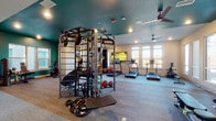 Located at 2818 Cullman Ave in Charlotte, NC, this single-floor fitness center is thoughtfully designed to support a wide range of workout routines. The space is divided into distinct functional zones, each outfitted with professional-grade equipment to serve various fitness needs.

The cardio area is lined with large windows that flood the room with natural light and offer views of the surrounding outdoors. TRUE brand treadmills and rowing machines are arranged along the windowed walls, providing an energizing environment for aerobic workouts. Ceiling fans overhead ensure comfortable airflow throughout.

At the heart of the facility sits a TKO multi-functional training rig, a versatile piece of equipment featuring cable attachments, pull-up bars, battle ropes, and an assortment of medicine balls — ideal for functional and strength-based training. The teal-painted ceiling in this zone creates a distinct visual identity, setting it apart from the lighter-toned areas of the center.

A dedicated strength training area houses a cable machine and adjustable bench, positioned near windows and glass doors that connect to the outdoor surroundings. The open layout of this zone allows for unobstructed movement.

The entry area features a clean, open floor plan with a built-in dual water fountain station, recessed lighting, and glass doors that enhance the sense of openness. Durable carpet tile flooring is used consistently throughout, providing traction and comfort underfoot.