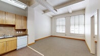 Located at 1003 Walnut St in the heart of Kansas City, MO, this two-bedroom, one-bathroom loft-style residence offers a distinctive urban living experience on a single floor. The space showcases a thoughtfully open layout with an industrial character defined by exposed cylindrical ductwork running across the ceiling, adding an authentic loft aesthetic throughout.

The living and kitchen area flow seamlessly together, with the kitchen featuring light wood cabinetry, a tile backsplash, white appliances including a refrigerator, range, microwave, and dishwasher, and durable tile flooring. The adjoining living area is carpeted and benefits from large windows that bring in generous natural light and offer views of the surrounding downtown cityscape.

The primary bedroom is a well-proportioned retreat with soaring ceilings, a ceiling fan, and a walk-in closet with built-in shelving. Its large windows frame urban views and fill the room with light. The second bedroom is equally bright, featuring dual windows with blinds, carpeted flooring, and a ceiling fan. Both rooms are connected via a carpeted hallway.

The bathroom is clean and functional, equipped with a full-size soaking tub and shower combination with chrome fixtures. Warm wood-toned baseboards are consistent throughout, tying the space together with a cohesive, welcoming finish.