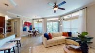 This single-story residence offers a thoughtfully designed open-concept layout connecting the living, dining, and kitchen areas into one cohesive living space. The living room is generously proportioned, featuring crown molding, a ceiling fan, and large windows that flood the room with natural light while framing views of surrounding greenery. A sliding glass door provides direct access to a private balcony, reinforcing the indoor-outdoor connection. The adjoining dining area accommodates a full-sized table and benefits from a pendant light fixture and additional window views of the tree canopy beyond.

The kitchen is well-equipped with rich dark wood cabinetry, granite countertops, stainless steel appliances, recessed lighting, and distinctive polished concrete flooring that extends throughout much of the unit. A dedicated pantry area adds practical storage.

Two bedrooms offer comfortable retreats, each featuring ceiling fans, crown molding, and ample natural light through large windows with sheer drapery. One bedroom includes its own exterior door access. The bathroom is spacious, featuring a wide double-sink vanity with dark wood cabinetry, a large walk-in glass-enclosed shower with tile surround, and pendant lighting, creating a clean, functional aesthetic throughout.