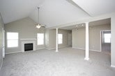 This single-floor residence is defined by a generously proportioned open-concept living area anchored by a pair of white decorative columns that lend architectural character to the space. Vaulted ceilings with ceiling fans enhance the sense of volume, while a fireplace with a white surround and multiple windows allow natural light to fill the room. Soft neutral carpet extends throughout the living and bedroom areas, complementing the warm, understated color palette of the walls.

The kitchen is well-appointed with white cabinetry, granite-style countertops, and a full suite of stainless steel appliances including a refrigerator, electric range with microwave above, and a peninsula that opens toward the living area. Wood-look tile flooring grounds the kitchen and extends into the bathrooms.

The bedrooms are carpeted and include ceiling fans; one features a tray ceiling detail and direct access to a private en-suite bathroom. A second bathroom offers a soaking tub with shower surround, white cabinetry, and granite-style countertops. A dedicated walk-in closet with wire shelving provides ample storage. A separate laundry area accommodates a full-size washer and dryer side by side, adding everyday convenience to the layout.