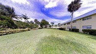 This single-story property is situated within a beautifully landscaped tropical setting, offering a serene and inviting outdoor environment. The grounds are defined by a generous, well-kept lawn that stretches openly, framed by a rich variety of mature palm trees, broad-leafed tropical plantings, and neatly trimmed hedges that lend the space a polished, resort-like character.

The building itself presents a clean, low-profile facade finished in a soft yellow tone, with evenly spaced windows that allow natural light to flow into the interior. Its single-story design contributes to an accessible, open feel that complements the surrounding landscape.

The outdoor grounds are a standout feature of this property. Towering palms and lush greenery create a canopy that provides both shade and a vibrant tropical ambiance. The wide expanse of manicured grass offers ample open space, ideal for leisurely outdoor activities or simply enjoying the surroundings.

Set beneath bright, open skies characteristic of a warm coastal climate, the overall atmosphere of this property is relaxed and sun-drenched. The combination of tropical flora, open lawns, and the understated architecture creates a cohesive and pleasant environment that is both visually appealing and functionally welcoming.