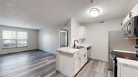 Located at 5400 Diamond Loch in Columbus, Ohio, this single-floor unit has been thoughtfully updated with contemporary finishes throughout. The open-concept living and kitchen area serves as the heart of the space, where light gray luxury vinyl plank flooring flows seamlessly underfoot, complemented by neutral-toned walls and textured ceilings. The kitchen is a standout feature, showcasing crisp white shaker-style cabinetry with matte black hardware, a marble-look countertop peninsula with an undermount sink and matte black faucet, and a full suite of stainless steel appliances including a refrigerator, electric range, and over-the-range microwave. The living area receives natural light through a window overlooking greenery, creating a warm and inviting atmosphere. A hallway connects the main living space to the additional rooms, including a bedroom finished with plush carpet and a window framing outdoor views. The bathroom is clean and modern, appointed with white cabinetry, a white countertop vanity, matte black hardware accents, a tub-shower combination, and coordinating vinyl plank flooring. Throughout the unit, the consistent use of light tones, updated fixtures, and quality finishes creates a cohesive, move-in-ready environment well-suited for comfortable everyday living.
