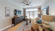 Located at 1100 S Main St in Greenville, South Carolina, this single-floor residence offers a thoughtfully designed layout with modern finishes and a cohesive contemporary aesthetic throughout.

The kitchen is a standout feature, showcasing rich dark-wood cabinetry extending floor to ceiling, stainless steel appliances including a range, microwave, and refrigerator, and clean white quartz countertops. A peninsula with bar seating provides an ideal transition into the living areas, with pendant lighting adding a refined touch. Wood-look flooring runs through the kitchen and common areas.

The living room is generously proportioned, bathed in natural light from large windows and a glass door that frames outdoor views. A ceiling fan, neutral tones, and hardwood-style flooring create a comfortable, welcoming atmosphere.

The bedrooms are carpeted and tranquil, each offering natural light through sizable windows with ceiling fans overhead. Walk-in closets provide ample storage, enhancing the functional appeal of each room.

The bathroom features dark cabinetry with white quartz counters, a framed mirror, and a tiled tub-shower combination. Wood-look flooring continues here, complementing the consistent design language found throughout the residence.