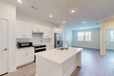Located at 100 Oakbrook Drive in McDonough, Georgia, this well-designed one-bedroom, one-bathroom residence offers a thoughtfully planned single-level layout with modern finishes throughout. The open-concept living area seamlessly connects the kitchen, dining, and living spaces, creating a bright and functional environment. The kitchen is a standout feature, equipped with crisp white shaker cabinetry, white quartz countertops, a subway tile backsplash, and a full suite of stainless steel appliances including a French door refrigerator, electric range, and microwave. A central island with an undermount sink provides additional prep space and casual dining options. Light wood-look flooring flows consistently throughout the unit, enhancing the clean, contemporary aesthetic. The bedroom offers a comfortable footprint, natural light through a window with exterior views, and a ceiling fan. Two closets, including a spacious walk-in with wire shelving systems, provide ample storage. The bathroom is generously sized, featuring a white vanity with quartz countertop, a tiled walk-in shower, and accessibility grab bars. Additional practical spaces include a pantry, laundry area, and utility room, rounding out the efficient and complete floor plan.