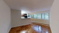 This 1-bedroom, 1-bathroom residence offers a thoughtfully organized single-floor layout that maximizes its comfortable footprint. The open living room is a standout feature, showcasing gleaming parquet wood flooring in a classic block pattern that extends throughout the home. A bank of wide windows lines the living area, allowing natural light to fill the space while offering views of the surrounding exterior. A ceiling fan adds both functionality and a finishing touch to the living room.

The kitchen is positioned adjacent to the living area and features rich, dark-stained cabinetry, granite-style countertops, a gas range, dishwasher, and a pass-through window that connects it to the main living space — ideal for casual interaction and easy serving. Light tile flooring completes the kitchen's clean, practical aesthetic.

The generously sized primary bedroom continues the parquet flooring theme and includes a built-in closet with bifold doors and a window that brings in natural light. The full bathroom is neatly appointed with a wood-toned vanity, white countertop, large mirror, and tile wall surround. Throughout the residence, neutral wall tones and consistent flooring create a cohesive, move-in-ready atmosphere.