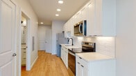 Located at 300 E Fifth Ave in Columbus, Ohio, this single-floor unit offers a clean, contemporary design throughout. The open-concept layout is anchored by light hardwood flooring that runs seamlessly from the entryway through the main living areas, creating a cohesive and airy feel.

The kitchen is a standout feature, outfitted with crisp white shaker cabinetry, light quartz countertops, and a classic white subway tile backsplash. Stainless steel appliances—including a refrigerator, electric range, built-in microwave, and dishwasher—are neatly integrated along the galley-style layout. Recessed lighting above illuminates the workspace efficiently.

A dedicated in-unit laundry closet provides convenient stacked washer and dryer access. Nearby, a spacious walk-in closet offers ample storage with built-in shelving and hanging rods. The bathroom features a glass-enclosed walk-in shower with floor-to-ceiling white tile and matte black hardware accents, lending a refined, modern touch.

The living area benefits from generous natural light, courtesy of large floor-to-ceiling windows with a black frame finish that frame views of the surrounding Columbus cityscape. The neutral wall palette and recessed lighting throughout the unit contribute to a bright, welcoming ambiance well-suited for modern urban living.