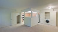 This single-floor residence features an open, airy layout designed to maximize functionality and flow. The living area is finished with neutral wall-to-wall carpeting that lends a soft, understated feel to the space, while bright white walls and a smooth ceiling contribute to an overall sense of openness and cleanliness.

A centrally positioned partial-wall divider separates the living area from the kitchen, incorporating a pass-through window that maintains visual connectivity between the two spaces. This architectural detail allows natural sightlines across the floor plan without fully opening the rooms to one another.

The kitchen is well-appointed with light wood cabinetry that extends to the upper walls, offering generous storage capacity. Stainless steel appliances, including a microwave and a gas range, are integrated into the layout. A white refrigerator and additional counter space round out the kitchen's practical offerings.

Multiple doorways lead to additional areas of the residence, with white panel doors providing clean transitions between rooms. The overall design is practical and understated, featuring consistent neutral tones and straightforward finishes throughout that create a cohesive, livable environment.