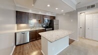 Located in Atlanta, GA, this efficiently designed one-bedroom, two-bathroom residence offers a thoughtful single-floor layout that maximizes every square foot. The kitchen serves as a standout centerpiece, showcasing rich dark cabinetry, granite countertops, a subway tile backsplash, and a full suite of stainless steel appliances including a dishwasher, range, microwave, and refrigerator. A granite-topped island provides additional prep space and separates the kitchen from the adjoining living area, which features warm hardwood-style flooring and recessed lighting throughout.

The bedroom is a comfortable retreat, finished with soft wall-to-wall carpeting, crown molding, and a ceiling fan. Natural light fills the room through windows framing views of surrounding greenery, contributing to a calm and airy atmosphere. A dedicated closet provides practical storage.

The two bathrooms are well-appointed: one features a full tub-shower combination with classic white tile surround and chrome fixtures, while the second includes a dark granite vanity with an undermount sink and dark wood cabinetry with hardwood-style flooring. A connecting hallway ties the layout together seamlessly. Crown molding and neutral tones throughout lend the space a cohesive, polished aesthetic.