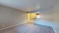 This single-floor unit offers a clean, functional layout with consistent light wood-look flooring throughout. The spacious living area features neutral-toned walls and connects seamlessly to the kitchen via an open pass-through with a dark granite-style countertop bar, creating an airy, open feel. A window near the entry door allows natural light to brighten the space.

The galley-style kitchen is well-appointed with dark wood cabinetry, dark granite-look countertops, white appliances including a refrigerator, electric range, and dishwasher, and a skylight overhead that floods the space with additional natural light.

The bedroom is a comfortable, well-proportioned room featuring a ceiling fan with light fixture, a large window with exterior views, and the same wood-look flooring that flows throughout the unit. The room offers ample wall space for flexible furniture arrangements.

The bathroom is accessed via a short hallway flanked by two doors, providing a sense of separation and privacy. The bathroom continues the light flooring theme and includes essential fixtures in a clean, straightforward layout.

Overall, the unit presents a practical and well-maintained living space with a cohesive neutral color palette, consistent flooring, and functional room connectivity throughout.