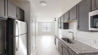 This contemporary one-bedroom, one-bathroom residence offers a thoughtfully designed single-floor layout that maximizes every square foot. Light hardwood-style flooring flows consistently throughout the unit, lending a clean, cohesive aesthetic across all rooms.

The galley-style kitchen is a standout feature, outfitted with dark espresso shaker cabinetry, granite countertops, a classic white subway tile backsplash, and a full suite of stainless steel appliances including a refrigerator, electric range, microwave, and dishwasher. A deep undermount sink with a modern gooseneck faucet completes the functional workspace.

The open living area receives natural light through a large window and is outfitted with a sleek ceiling fan, creating a bright and airy atmosphere. The spacious primary bedroom offers generous room to accommodate a full furniture arrangement, with soft neutral walls and continued hardwood-style flooring.

The bathroom features dark cabinetry paired with granite countertops, an undermount sink, a wide vanity mirror, and chrome fixtures, maintaining the modern design language found throughout the home. A hallway connects the main living spaces, providing a smooth and logical flow between rooms. The overall palette of whites, grays, and warm wood tones gives the unit a fresh, contemporary character.