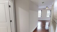 Located in the heart of Norfolk, VA, this well-appointed one-bedroom, one-bathroom unit on Granby Street offers a thoughtfully designed layout across a single floor. Rich, dark hardwood flooring flows throughout the main living areas, creating a warm and cohesive aesthetic. The open-concept living, dining, and kitchen area serves as the focal point of the unit, maximizing the use of space. The kitchen is a standout feature, equipped with stainless steel appliances including a range, microwave, and refrigerator, complemented by dark espresso cabinetry with glass-front upper panels, a white quartz countertop with an undermount stainless steel sink, a sleek tile backsplash, and stylish pendant lighting overhead. The bedroom offers a cozy retreat with a window for natural light, a ceiling fan, direct access to the bathroom, and a closet. The bathroom is cleanly finished with large-format neutral tile flooring and walls, a soaking tub with shower, and a dark-cabineted vanity with white countertop. A dedicated laundry area with wire shelving and washer/dryer hookups adds practical convenience. Neutral wall tones and crisp white trim throughout give the space a clean, modern feel.