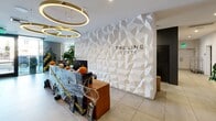 The Line Lofts lobby is a thoughtfully designed single-floor space that balances contemporary aesthetics with warm, inviting elements. At its focal point stands a dramatic three-dimensional geometric feature wall finished in white, bearing the property's branding and serving as an eye-catching architectural centerpiece. Oversized circular pendant lights cast a warm glow over the reception desk, which is set against dark cabinetry accented with rich black marble countertops.

Large floor-to-ceiling windows along the street-facing wall flood the space with natural light, framing views of the tree-lined exterior. Beneath these windows, a built-in wood banquette seating area is paired with a marble-topped table and curved leather chairs, creating an intimate lounge nook. Exposed concrete walls add an industrial contrast to the warmth of the wood paneling found throughout.

Large-format porcelain tile flooring extends across the entire space, providing a clean, cohesive foundation. Lush potted plants, including fiddle-leaf figs and scheffleras, are positioned throughout, introducing a vibrant natural element. A glass-partitioned workspace with draped linen curtains offers a private yet accessible area within the lobby. The overall ambiance is polished and modern, with carefully curated details that create a welcoming, upscale environment.