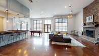 Located at 2501 S 4th St in Louisville, Kentucky, this single-floor amenity space is thoughtfully designed to offer a variety of functional and social environments. Throughout, polished concrete floors in warm amber tones provide a cohesive foundation, complemented by a neutral color palette and contemporary furnishings.

The main lounge area is expansive and light-filled, featuring large black-framed windows that frame views of the surrounding community. A striking herringbone brick fireplace with a dark wood mantel serves as a focal point, flanked by stylish accent chairs and a wall-mounted TV, creating an inviting gathering spot. A billiard table and bar-height seating add a recreational dimension to the space.

A dedicated bar area features a long dark-wood counter, industrial pendant lighting, paneled cabinetry, and mounted screens — ideal for social events or casual meetings. Adjacent seating areas with modular sofas, a round dining table, and patterned accent chairs provide flexible spaces for conversation and collaboration.

The business center offers a focused work environment, lined with built-in desks, multiple computer workstations, and bold blue accent walls. Private rooms with glass-paneled doors provide quieter settings for meetings or individual use. Clerestory windows in select areas draw in additional natural light, enhancing the space's airy, modern atmosphere throughout.