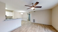This single-story unit offers a clean, modern aesthetic anchored by light wood-style flooring that runs consistently throughout the living areas, kitchen, and bedroom. Neutral warm-gray walls create a cohesive, understated backdrop across every room.

The open living area is spacious and well-lit, featuring a ceiling fan with integrated lighting and a sliding glass door dressed with vertical blinds that allows natural light to flow in while providing access to an outdoor area. A pass-through counter connects the living space to the kitchen, enhancing the open feel.

The galley-style kitchen is efficiently designed with granite countertops on both sides, white upper cabinetry, gray lower cabinetry, and a full suite of stainless steel appliances including a refrigerator, electric range, and over-the-range microwave. A set of louvered bifold doors provides convenient pantry storage, and a skylight-style overhead fixture brightens the space.

The bedroom is comfortably sized with a window that brings in natural light and views of surrounding greenery. The bathroom is finished with granite-topped vanity cabinetry, a full tub-shower combination with white tile surround, and brushed nickel hardware, maintaining the unit's consistent, polished style.