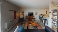 This 1-bedroom, 1-bathroom unit is laid out on a single floor, offering a practical and comfortable living arrangement. The living room serves as the central gathering space, featuring wood-look flooring, neutral gray walls, and a sliding glass door with vertical blinds that allows natural light to pour in and provides access to an outdoor area. A wall-mounted air conditioning unit ensures year-round comfort, while baseboard heating runs along the perimeter of the room.

The kitchen is outfitted with granite countertops, white cabinetry, a double undermount stainless steel sink, and stainless steel appliances, providing a clean and modern workspace. The layout connects seamlessly to the living and dining area, which includes bar-height seating for casual meals.

The bedroom is carpeted and comfortably sized, featuring a sliding-door closet with built-in shelving and hanging storage, offering ample organization. A window with horizontal blinds allows natural light while maintaining privacy.

The bathroom features the same granite countertop found in the kitchen, complemented by an undermount sink, dark cabinetry, and wood-look tile flooring. A shower-tub combination with a curtain and a window above the toilet adds both function and light to the space. Overall, the unit presents a cohesive, updated aesthetic throughout.