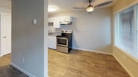 This single-floor unit presents a straightforward and functional layout designed for comfortable everyday living. Throughout the space, wood-look plank flooring in warm, natural tones creates a cohesive and inviting aesthetic, complemented by neutral-toned walls and white baseboards. Textured ceilings add a classic finishing detail consistent across all rooms.

The living area is well-proportioned, featuring large windows fitted with horizontal blinds that allow natural light to filter in. A front entry door with adjacent windows enhances the sense of openness. Baseboard heaters are present along the walls, providing efficient zone heating throughout the unit.

The kitchen is cleanly appointed with white shaker-style cabinetry, a stainless steel electric range, an under-cabinet range hood, and a sink with a light stone-toned countertop. A ceiling fan with a light fixture serves the adjacent area, improving air circulation. The layout appears open to the main living space, allowing for easy flow between cooking and living areas.

The bathroom offers a full tub-shower combo with a curved curtain rod, a white vanity with grey countertop, and matching wood-look flooring that ties the space together with the rest of the unit. The overall design is clean, updated, and move-in ready.