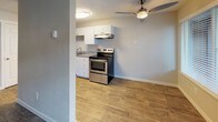 This single-floor unit presents a straightforward and functional layout designed for comfortable everyday living. Throughout the space, wood-look plank flooring in warm, natural tones creates a cohesive and inviting aesthetic, complemented by neutral-toned walls and white baseboards. Textured ceilings add a classic finishing detail consistent across all rooms.

The living area is well-proportioned, featuring large windows fitted with horizontal blinds that allow natural light to filter in. A front entry door with adjacent windows enhances the sense of openness. Baseboard heaters are present along the walls, providing efficient zone heating throughout the unit.

The kitchen is cleanly appointed with white shaker-style cabinetry, a stainless steel electric range, an under-cabinet range hood, and a sink with a light stone-toned countertop. A ceiling fan with a light fixture serves the adjacent area, improving air circulation. The layout appears open to the main living space, allowing for easy flow between cooking and living areas.

The bathroom offers a full tub-shower combo with a curved curtain rod, a white vanity with grey countertop, and matching wood-look flooring that ties the space together with the rest of the unit. The overall design is clean, updated, and move-in ready.