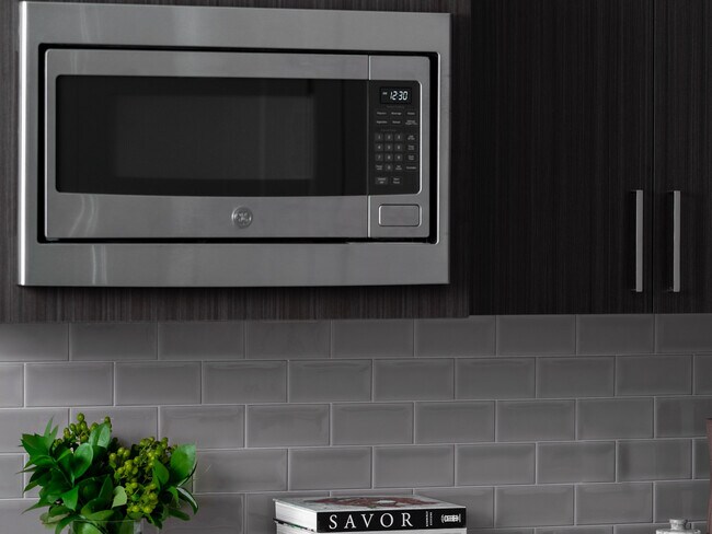 Elegante cocina con un elegante microondas de acero inoxidable GE, modernos gabinetes de madera oscura de cierre lento y un elegante protector contra salpicaduras de azulejos tipo metro. - 30 Court Street Apartments