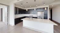 Located in the heart of Dallas's vibrant Uptown neighborhood, this modern single-floor residence at 2803 Cole Ave offers a sleek, contemporary design with high-end finishes throughout. The open-concept living area is bathed in natural light, featuring light hardwood flooring and expansive floor-to-ceiling windows and sliding glass doors that open to a private balcony with sweeping Dallas skyline views.

The chef's kitchen is a standout feature, showcasing dark espresso cabinetry, crisp white quartz countertops, a large center island with an undermount sink, stainless steel appliances including a French door refrigerator and built-in microwave, and stylish pendant lighting overhead.

The bedroom continues the refined aesthetic with plush carpeting, sliding glass door balcony access, and generous natural light framing panoramic city views. Two walk-in closets with built-in shelving and hanging rods provide ample storage.

The bathrooms are finished with elegance, featuring a soaking tub surrounded by large-format stone-look tile with a built-in niche, a glass-enclosed walk-in shower, backlit vanity mirror, dark cabinetry, and light tile flooring. A dedicated laundry area with full-size front-loading washer and dryer and overhead cabinetry adds practical convenience to this refined urban residence.