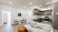 Located at 418 N Norton Ave in Los Angeles, this single-story home offers an impressive eight bedrooms and three bathrooms within a thoughtfully designed, modern layout. Light wood-style flooring runs throughout, complementing the clean white walls and recessed lighting that give the space a bright, contemporary feel.

The open-concept living and kitchen area serves as the heart of the home. The kitchen is well-appointed with dark wood cabinetry, white quartz countertops, a textured tile backsplash, and a full suite of stainless steel appliances including a gas range, microwave, and French door refrigerator. The living area provides ample room for seating and entertainment, with a wall-mounted TV and space for a dining setup.

The eight bedrooms range in size, with the primary bedroom offering generous proportions. Several rooms feature large sliding glass doors or wide windows that invite natural light and outdoor views, enhancing the airy atmosphere. The bedrooms are finished with the same light hardwood flooring and crisp white walls.

The three bathrooms are modern and well-finished. One features a soaking tub with striking geometric textured tile surround, while another showcases decorative patterned floor tile paired with a wood-toned floating vanity and a combined tub-shower. Clean lines and neutral palettes define each bathroom's design. Two hallways connect the space efficiently, making this home as functional as it is stylish.