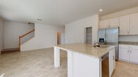 Located at 437 San Lorenzo Ct in Bradenton, Florida, this two-story home presents a clean, modern design with a bright, neutral palette throughout. The main level is anchored by an open-concept living and kitchen area, where large-format tile flooring extends seamlessly across the space. Vaulted ceilings in the living area enhance the sense of openness, while multiple windows fitted with horizontal blinds allow natural light to fill the room. A staircase with warm wood-toned railings connects the two floors.

The kitchen is well-appointed with white shaker-style cabinetry, granite countertops, a center island with a built-in sink, and stainless steel appliances including a refrigerator with ice maker, microwave, and range. Recessed lighting illuminates the space efficiently. A half bathroom on the main level features a pedestal sink with chrome fixtures and tile flooring. A dedicated laundry room accommodates a full-sized washer and dryer with overhead shelving and a window.

The upper level features carpeted bedrooms, each with closet access. The attached garage offers generous space with concrete flooring, an automatic opener, and direct interior access, completing this functional Florida home.