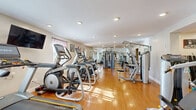 Located at 2184 Stratford Ave in Hatfield, PA, this single-floor fitness center offers a generously sized, fully equipped space designed to support a wide range of workout routines. The main exercise room is bright and open, featuring warm hardwood-style flooring and recessed lighting throughout that create an energizing yet clean aesthetic. Large wall mirrors amplify the sense of space and allow users to monitor their form during workouts.

The exercise room is outfitted with an extensive array of commercial-grade equipment, including multiple Hoist strength machines, cable systems, and multi-functional units for targeted muscle training. Cardio equipment — including treadmills, elliptical trainers, and stair climbers — lines the perimeter, while a dedicated open area accommodates functional training with stability balls, kettlebells, and a folding mat. A whiteboard on the wall suggests use for instructional or personal training sessions.

Natural light filters in through curtained windows, complementing the recessed lighting for a well-lit environment at any time of day. A clean, neutral color palette with crisp white walls maintains a professional and focused atmosphere. The facility also includes a convenient hallway and a private bathroom with classic black-and-white checkered tile flooring, ensuring a complete and self-contained fitness experience.