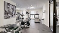 Located at 2750 Carousel Cres in Ottawa, Ontario, this fitness centre offers a well-organized and fully equipped exercise space designed to support a variety of workout routines. The room features durable rubber tile flooring throughout, providing a safe and practical surface for exercise. Recessed pot lights, along with flush-mount ceiling fixtures, deliver consistent, even illumination across the entire space.

The fitness centre is outfitted with a range of cardio equipment, including treadmills, an elliptical trainer, and a stationary bike, catering to different cardiovascular training preferences. A multi-station cable weight machine with an accompanying bench provides dedicated strength training options. Motivational fitness posters and a posted fitness centre rules sign contribute to an organized, purposeful atmosphere.

A large wall mirror runs along one side of the room, visually expanding the space and allowing users to monitor their form during workouts. A window along the exterior wall introduces natural light and provides ventilation support alongside a wall-mounted air conditioning unit. The space is accessed through frosted glass sliding doors, offering both privacy and a clean, modern aesthetic. Overall, the fitness centre is a practical, no-frills amenity designed to meet residents' essential health and wellness needs.