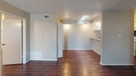 This single-floor residence offers a thoughtfully laid-out interior highlighted by rich, dark hardwood-style flooring that flows consistently throughout every room, creating a warm and cohesive aesthetic. The living room is a standout area, featuring a vaulted ceiling that adds a sense of height and openness, a classic wood-paneled fireplace as a focal point, and a window that invites natural light. Adjacent to the living area, a dining or flex space connects seamlessly to the kitchen via a pass-through counter, enhancing the open feel of the common areas. A skylight in the transition area further brightens the interior. The kitchen is equipped with white cabinetry, granite-style countertops, a full-size refrigerator, an electric range, and a striking mosaic tile backsplash that adds a decorative touch. The bedroom is generously proportioned, featuring a ceiling fan with light fixture, a window for natural light, and direct access to the bathroom. The bathroom includes a granite-topped vanity with white cabinetry, a large mirror, and a full tub-shower combination. Textured ceilings are present throughout, and neutral wall tones provide a clean, move-in-ready canvas. The space also features ample closet storage and centralized HVAC venting throughout.