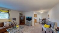 Located at 131 Kings Park Dr in Liverpool, NY, this single-floor residence offers a thoughtfully laid-out 2-bedroom, 1-bathroom floor plan with a comfortable, neutral aesthetic throughout. The open living and dining area forms the heart of the home, featuring soft carpeting, large windows that invite natural light, and ample room for both relaxing and entertaining. The living space flows seamlessly toward the kitchen, which is equipped with warm wood cabinetry, light countertops, tile flooring, and a window above the sink that brightens the room. The adjacent dining area provides a cozy setting with enough space for a full dining set. The primary bedroom is generously sized, offering a ceiling fan, a window with outdoor views, and comfortable carpet flooring. The second bedroom is equally well-lit and comfortable. A versatile office space adds flexibility, ideal for a home workspace or hobby room. The full bathroom features a window for natural ventilation and light. Three closets throughout the residence provide excellent storage. A connecting hallway ties the rooms together in a clean, functional layout, making this a well-organized and welcoming home.