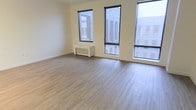 This single-floor space offers a clean and modern aesthetic, thoughtfully designed to maximize comfort and functionality. The main living area is immediately welcoming, featuring light-toned, hardwood-style flooring that runs seamlessly throughout, adding warmth and a contemporary feel to the interior.

Large, floor-to-ceiling black-framed windows are a standout architectural feature, flooding the space with generous amounts of natural light while offering views of the surrounding exterior. The multiple windows create an open, airy atmosphere that enhances the sense of spaciousness within the room.

The walls are finished in a soft, neutral cream tone that complements the flooring and contributes to the space's bright and inviting ambiance. A white baseboard heating unit is neatly positioned beneath one of the windows, ensuring practical climate control without disrupting the room's clean visual lines.

The overall design of the space is minimalist and versatile, providing a blank canvas well-suited for a variety of uses and furnishing arrangements. The combination of natural light, neutral finishes, and modern flooring makes this a functional and visually appealing space that is both comfortable and easy to personalize.