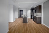 Located on the 9th floor at 66 Weber St E in Kitchener, Ontario, this one-bedroom, one-bathroom unit offers a well-designed open-concept layout with modern finishes throughout. Light-toned hardwood-style flooring runs continuously through the living, dining, and kitchen areas, creating a cohesive and bright interior complemented by recessed pot lighting and crisp white walls.

The kitchen is a standout feature, showcasing rich dark wood cabinetry paired with quartz countertops, a large central island with an undermount sink, and stainless steel appliances including a refrigerator, range, and microwave. A white subway tile backsplash adds a clean, modern touch. The open layout allows the kitchen to flow naturally into the living area, making the space feel generous despite its compact footprint.

The bedroom is a comfortable, enclosed space featuring a sliding door that opens to city views, allowing ample natural light. The bathroom is finished with a quartz vanity, dark wood cabinetry, chrome fixtures, and a large frameless mirror. Throughout the unit, two-panel white doors with black hardware provide a contemporary contrast. The overall ambiance is clean, modern, and efficiently designed for urban living.